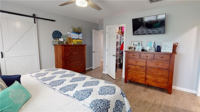 bedroom with light hardwood / wood-style floors, a barn door, ceiling fan, a closet, and a spacious closet