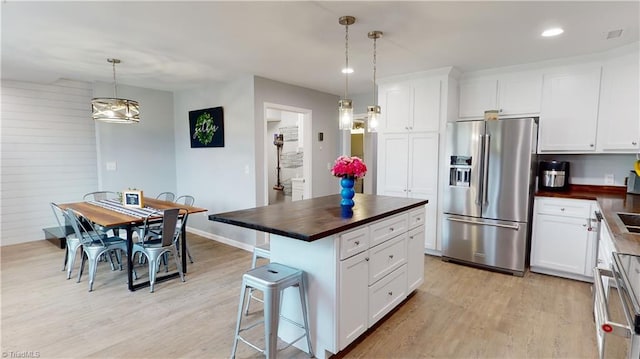 kitchen featuring white cabinets, light hardwood / wood-style flooring, a center island, pendant lighting, and stainless steel fridge