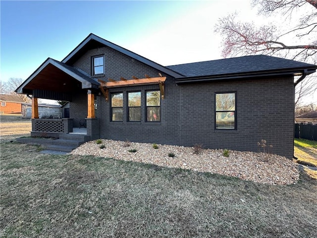 view of front of house with a shingled roof, a front yard, and brick siding