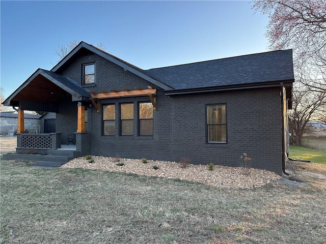 view of front of home featuring brick siding, roof with shingles, and a front yard