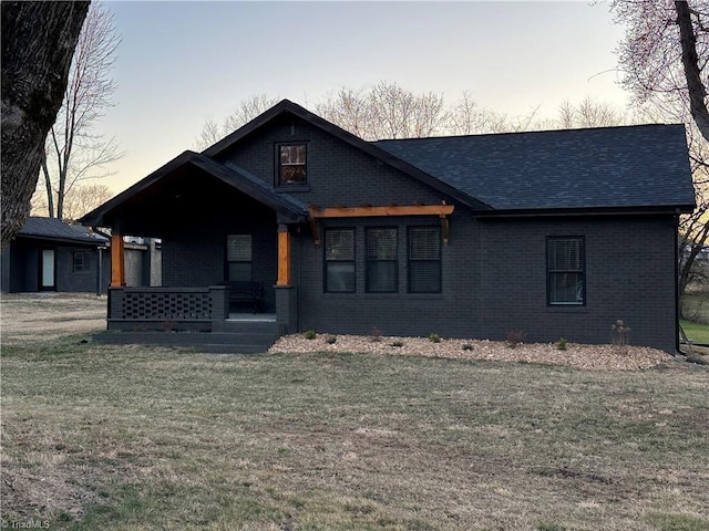 view of front facade with a porch, brick siding, a lawn, and a shingled roof