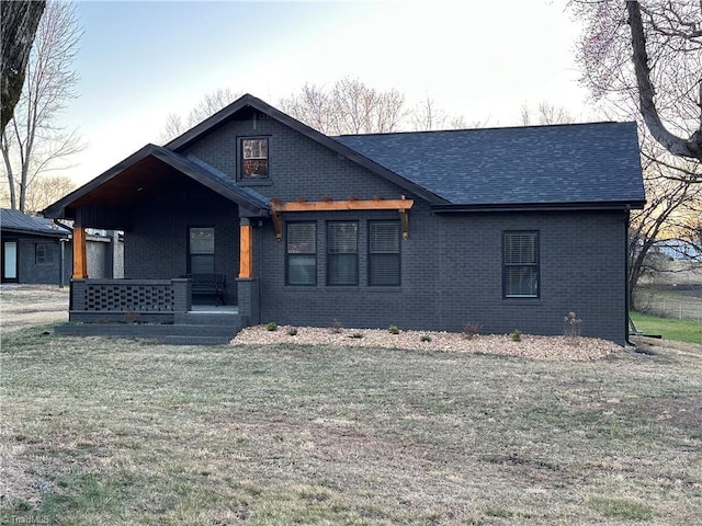 view of front facade featuring a shingled roof, a front lawn, a porch, and brick siding