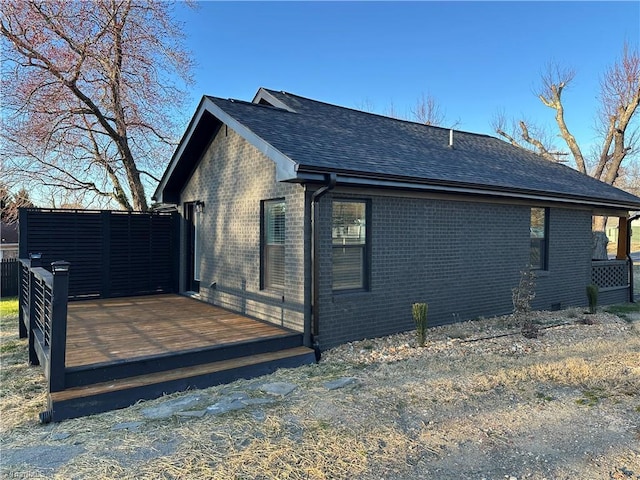 view of home's exterior with brick siding, a wooden deck, and roof with shingles