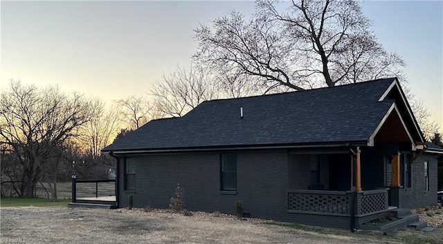 back of house with covered porch, brick siding, and roof with shingles