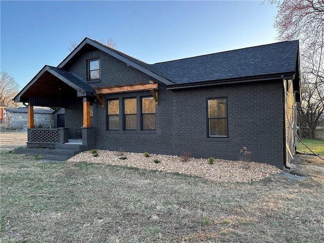 view of front facade featuring roof with shingles, brick siding, and a front lawn