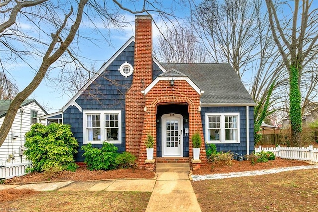 view of front of property with a shingled roof, a chimney, and fence