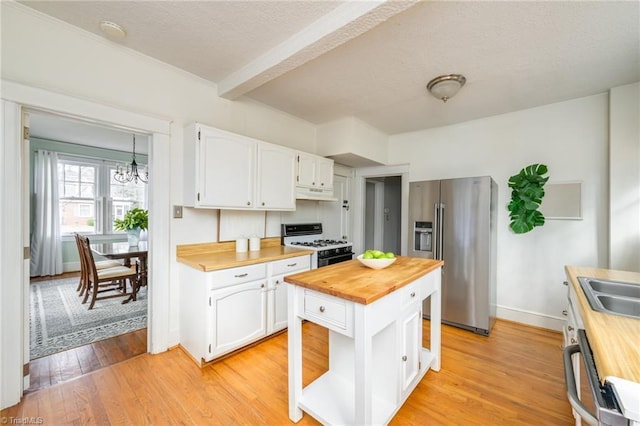 kitchen with high end fridge, white gas range oven, under cabinet range hood, wood counters, and white cabinetry