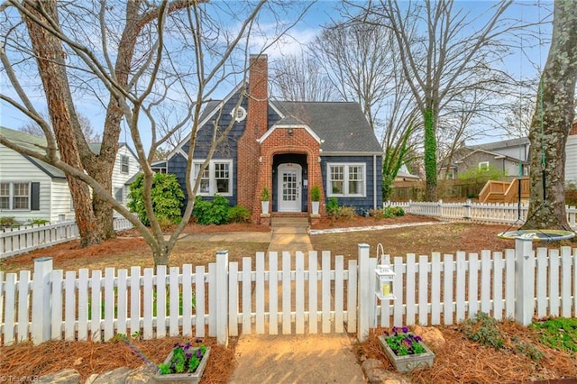 view of front of home featuring a shingled roof, brick siding, a fenced front yard, and a chimney