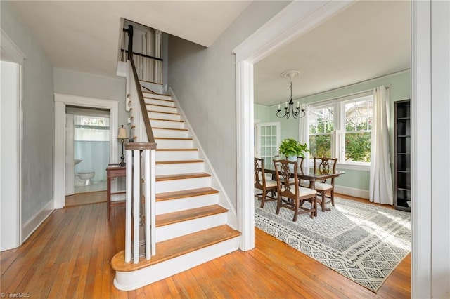 stairs with baseboards, wood-type flooring, and an inviting chandelier