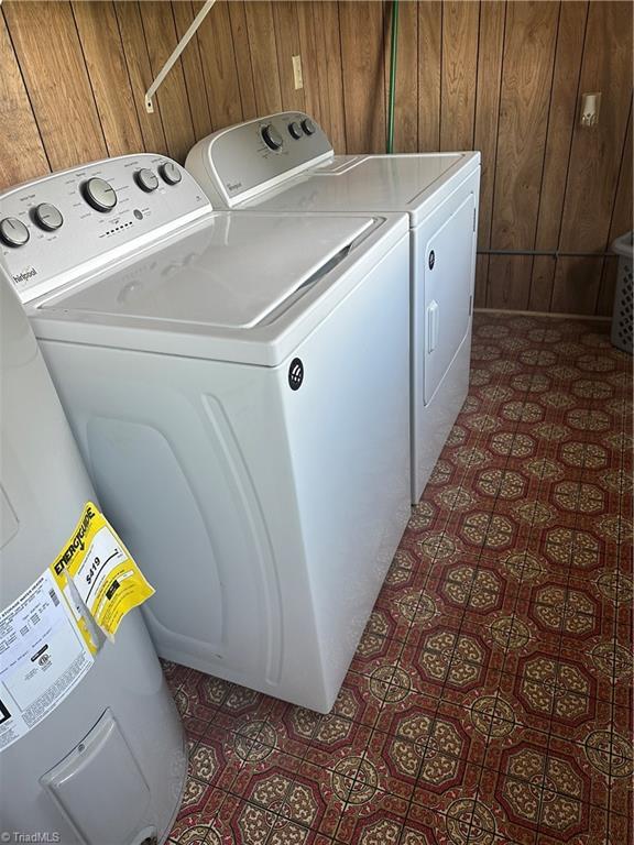 clothes washing area featuring wooden walls, dark floors, laundry area, and washer and clothes dryer