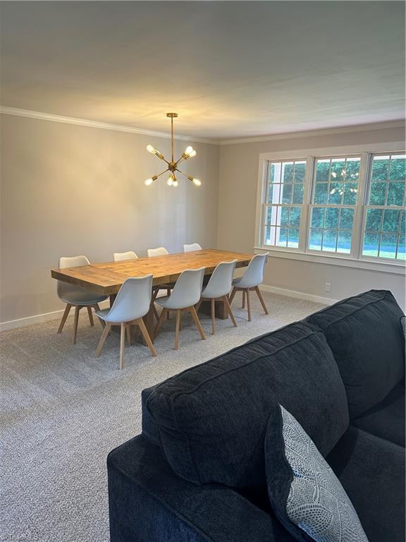 carpeted dining area with ornamental molding, a wealth of natural light, and an inviting chandelier