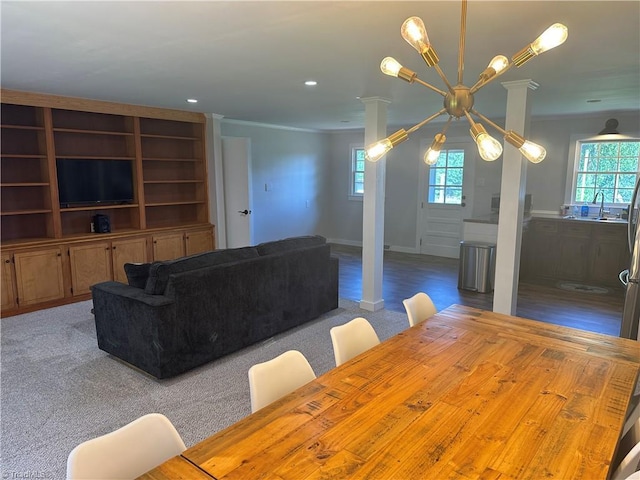 carpeted dining room featuring crown molding, plenty of natural light, decorative columns, and a sink
