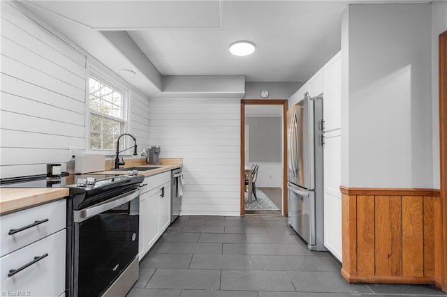 kitchen with white cabinetry, sink, wooden walls, and stainless steel appliances