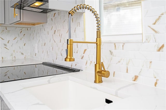 room details with sink, gray cabinetry, light stone counters, range hood, and backsplash