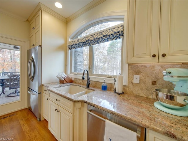 kitchen with sink, light stone counters, cream cabinetry, appliances with stainless steel finishes, and light wood-type flooring