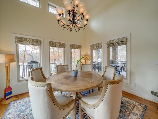 dining area with light hardwood / wood-style floors, a towering ceiling, a healthy amount of sunlight, and a notable chandelier