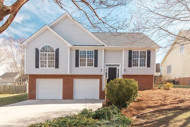 bi-level home featuring driveway, brick siding, an attached garage, and fence