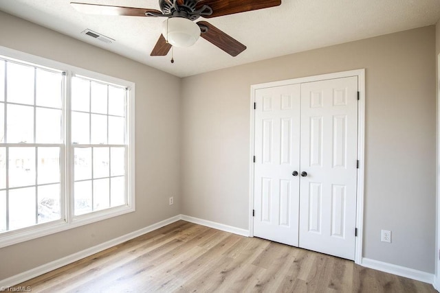 unfurnished bedroom featuring light wood-style floors, multiple windows, visible vents, and a closet