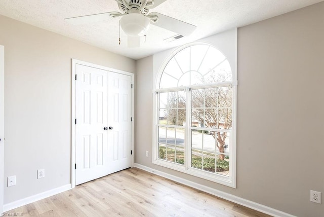 unfurnished bedroom featuring a textured ceiling, light wood-style flooring, visible vents, and baseboards