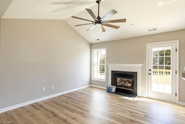 unfurnished living room featuring light wood-style floors, vaulted ceiling, plenty of natural light, and a fireplace with flush hearth