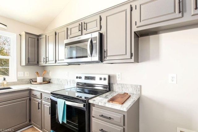 kitchen with lofted ceiling, appliances with stainless steel finishes, light countertops, and gray cabinetry