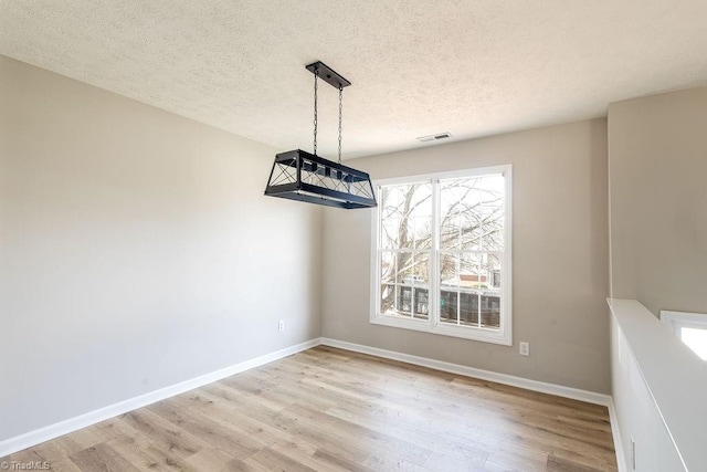 unfurnished dining area with visible vents, a textured ceiling, baseboards, and wood finished floors