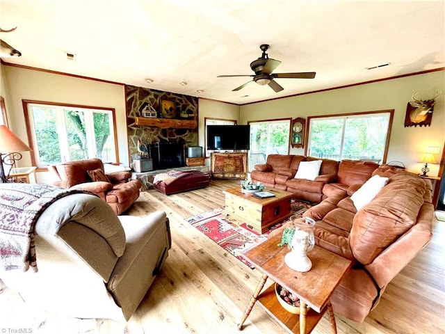 living room with ceiling fan, light hardwood / wood-style flooring, crown molding, and a stone fireplace