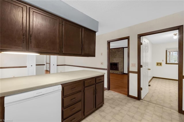 kitchen featuring dishwasher, dark brown cabinetry, and a brick fireplace