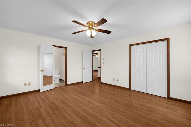 unfurnished bedroom featuring wood-type flooring, a closet, ensuite bath, and ceiling fan