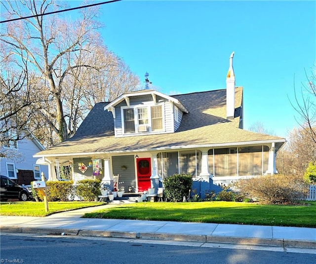 view of front of property featuring a front lawn, a chimney, a porch, and a sunroom