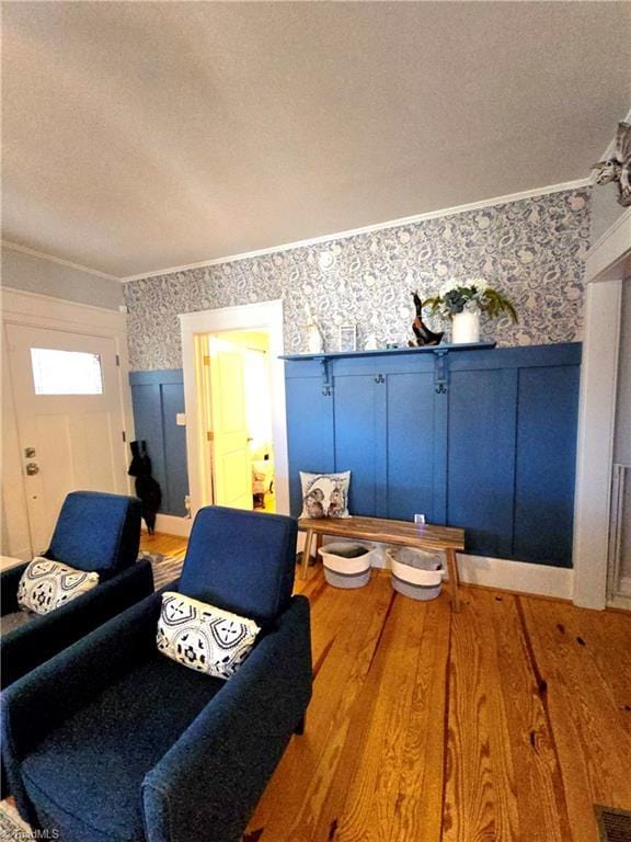 living area with a textured ceiling, crown molding, wood finished floors, and wallpapered walls