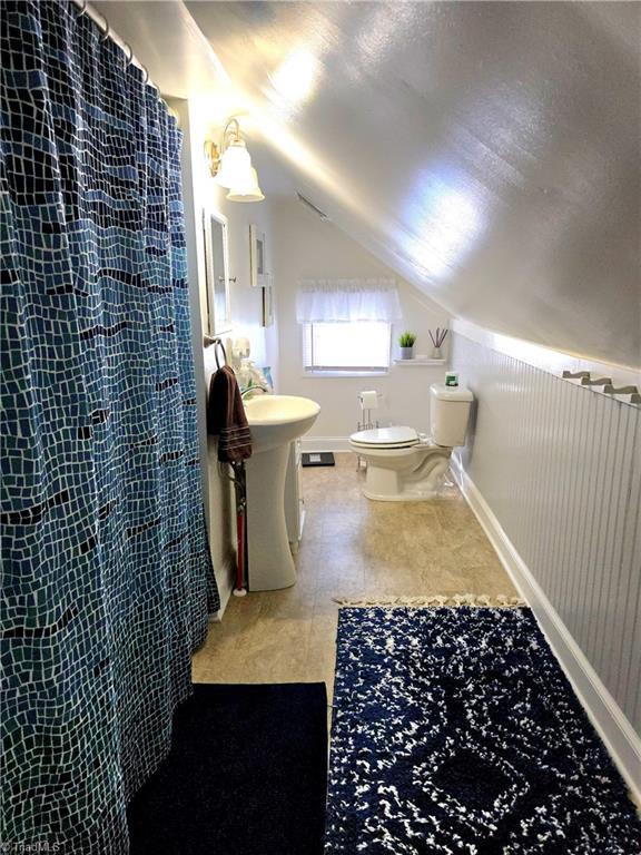 bathroom featuring lofted ceiling, baseboards, toilet, and a shower with curtain