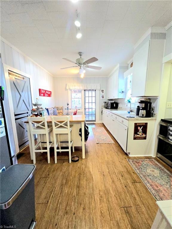 kitchen with crown molding, light wood finished floors, white cabinetry, a sink, and range