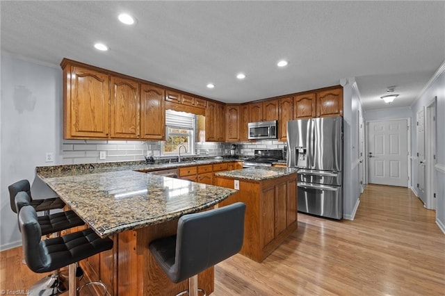 kitchen featuring a kitchen breakfast bar, dark stone countertops, light wood-type flooring, a kitchen island, and stainless steel appliances