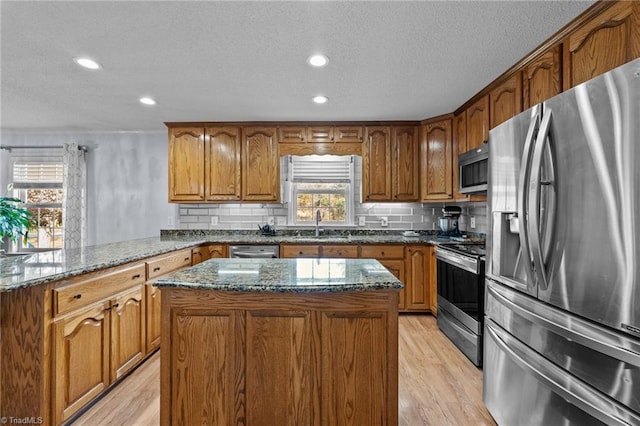 kitchen with dark stone countertops, light hardwood / wood-style floors, decorative backsplash, a kitchen island, and appliances with stainless steel finishes