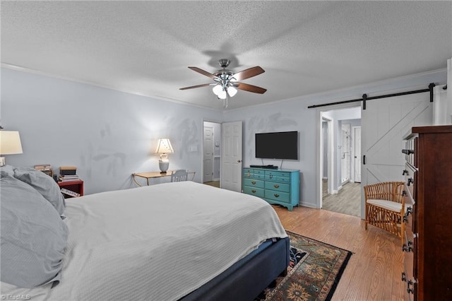 bedroom with light wood-type flooring, a textured ceiling, ceiling fan, crown molding, and a barn door