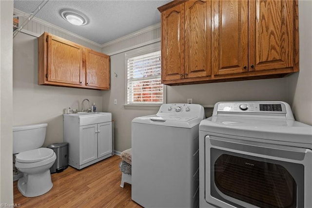 laundry area featuring a textured ceiling, crown molding, sink, independent washer and dryer, and light hardwood / wood-style floors