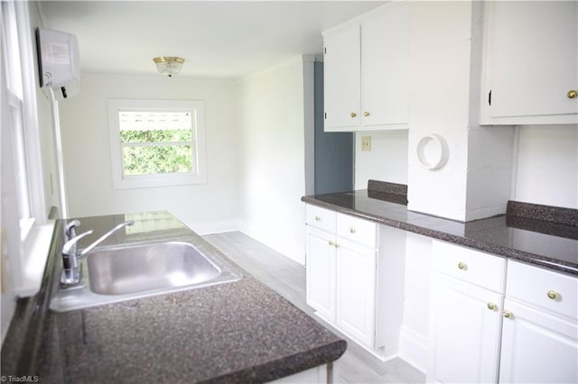 kitchen featuring light wood-style floors, dark stone counters, a wall mounted AC, white cabinets, and a sink