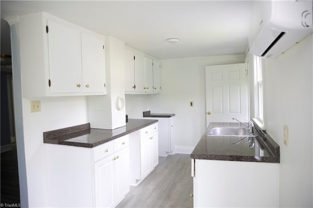 kitchen with baseboards, a wall mounted air conditioner, white cabinets, a sink, and light wood-style flooring