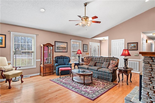 living area with visible vents, ceiling fan, vaulted ceiling, a textured ceiling, and wood finished floors