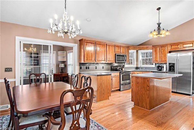 kitchen with lofted ceiling, stainless steel appliances, light wood-style floors, a chandelier, and a sink