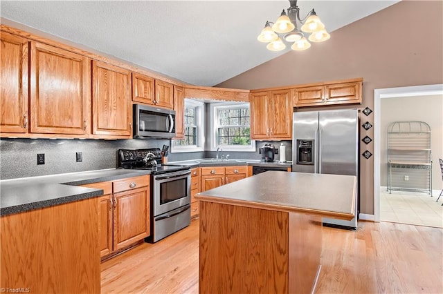 kitchen with a kitchen island, light wood-style floors, vaulted ceiling, appliances with stainless steel finishes, and dark countertops