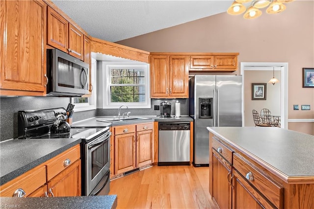 kitchen with a sink, vaulted ceiling, appliances with stainless steel finishes, light wood finished floors, and brown cabinetry