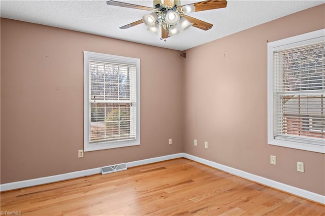 spare room featuring visible vents, light wood finished floors, baseboards, and a textured ceiling