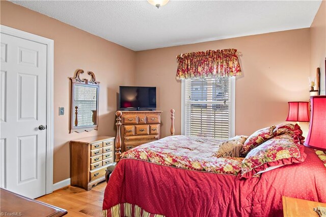 bedroom with baseboards, light wood-style flooring, and a textured ceiling