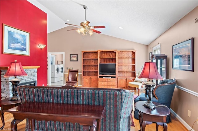 living area with ceiling fan, a stone fireplace, wood finished floors, vaulted ceiling, and independent washer and dryer