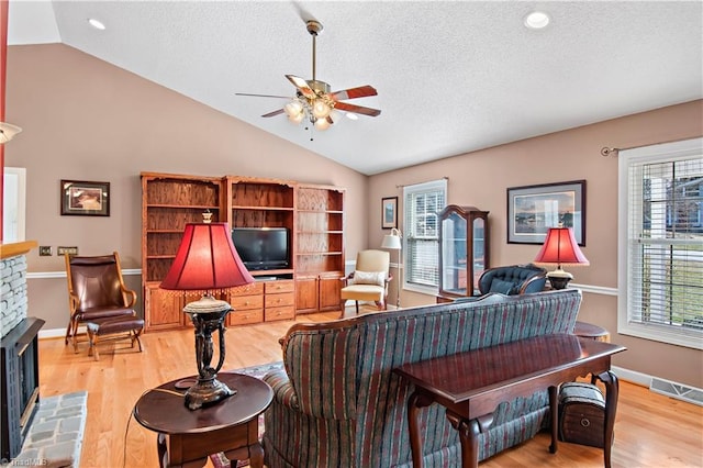 living room with lofted ceiling, a stone fireplace, light wood-style flooring, and a ceiling fan