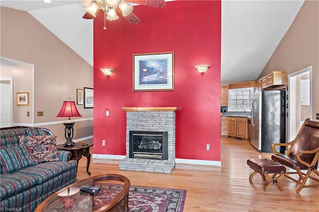 living area featuring high vaulted ceiling, light wood-style flooring, a fireplace, and baseboards