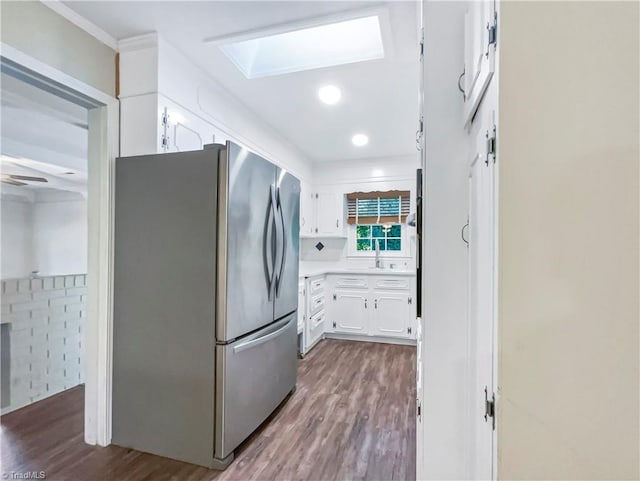 kitchen with hardwood / wood-style floors, stainless steel fridge, white cabinets, and a skylight