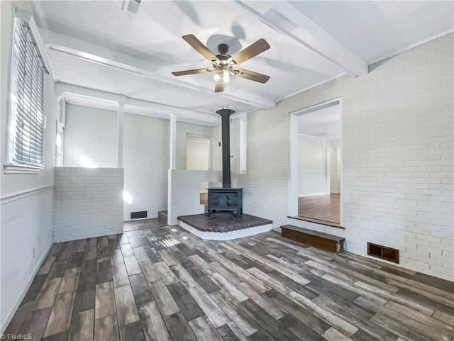 unfurnished bedroom featuring a wood stove, brick wall, beamed ceiling, and dark hardwood / wood-style flooring